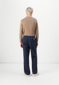 Brown long-sleeve sweater paired with navy blue trousers, featuring a relaxed fit and back pockets, set against a plain white background.