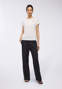 Top chiaro a maniche corte con ricamo floreale sulla spalla, abbinato a pantaloni neri a gamba larga e sandali flat.