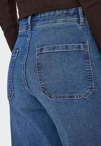 Tamnoplave traperice uskog kroja, sa dva stražnja džepa, visokim strukom i kontrastnim šavovima duž šavova.