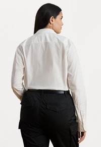 Biała koszula z długim rękawem o klasycznym kołnierzyku, z zapięciem na guziki przy mankietach oraz gładką teksturą, w połączeniu z czarnymi spodniami cargo z tylnymi kieszeniami.