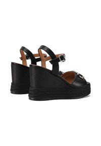 Sandali wedge neri in pelle con una texture intrecciata, cinturino alla caviglia regolabile e un dettaglio circolare sulla parte superiore.