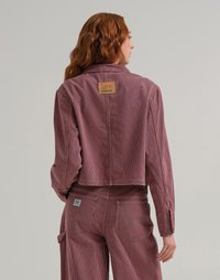 Giacca cropped a righe rosse e blu in corduroy, con un'etichetta quadrata sul retro e polsini con bottoni. Visibili pantaloni abbinati.