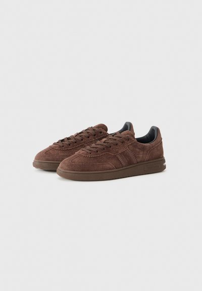 Brown suede sneakers with a low profile, round toe, and flat rubber sole. Features tonal laces and a slightly padded collar.