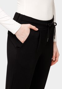 Zwarte joggingsbroek met een zachte textuur, voorzien van een elastische tailleband, trekkoordsluiting en zijzakken. Eenvoudig en functioneel ontwerp.