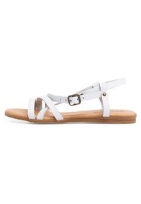Sandali bianchi in pelle con cinturini incrociati, fibbia regolabile alla caviglia e suola piatta marrone. Texture liscia e design minimalista.