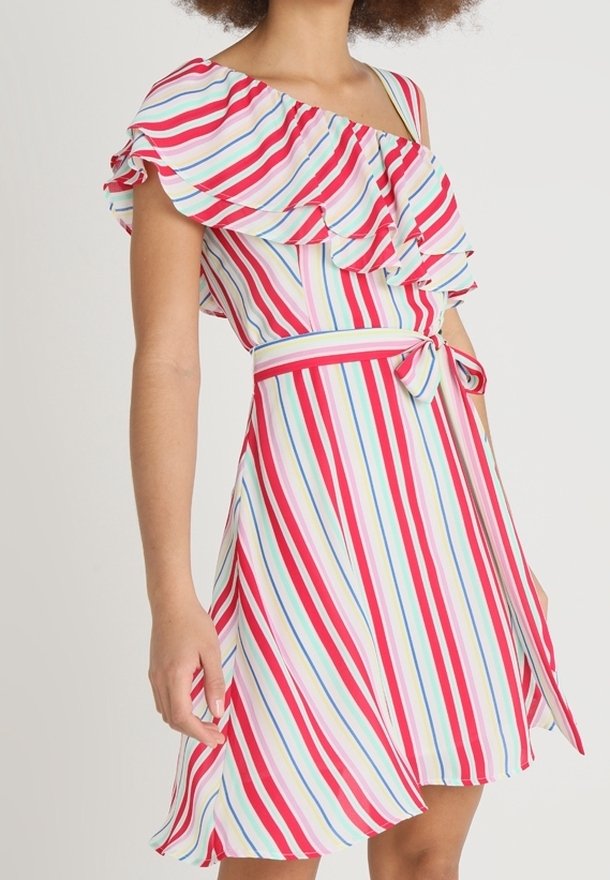 Femme portant une robe sans manches, à une épaule, avec des volants et des rayures verticales rouges, blanches, bleues et roses, nouée à la taille avec un nœud.