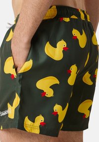 Groene zwemshorts met een patroon van rubberen eendjes. Voorzien van een elastische tailleband en zijzakken. Gemaakt van gladde, lichte stof.