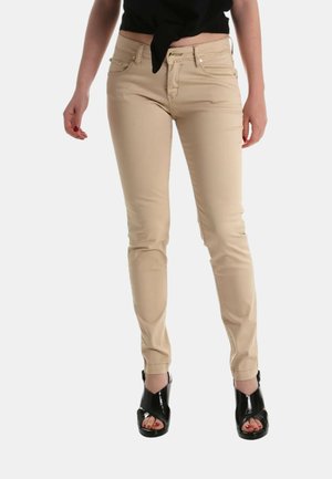 Pantaloni skinny beige con una texture liscia, dotati di chiusura con bottone, tasche frontali e una vestibilità slim. Abbinati a tacchi aperti neri.