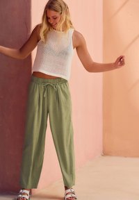 Hvid net-crop top kombineret med løstsiddende, olivengrønne linnedbukser. Outfit'et har en snøre i taljen og flade hvide sandaler.