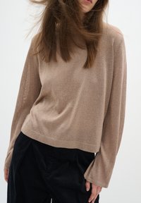 Maglia a maniche lunghe marrone chiaro con una vestibilità ampia e rilassata, realizzata in morbido materiale testurizzato. Presenta un'ampia scollatura e polsini a coste.