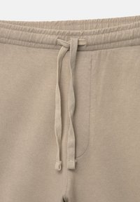 Pantaloni jogger din bumbac bej, cu talie elastică și șnur; au buzunare laterale și o textură netedă.