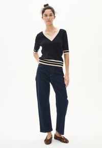 Schwarzes V-Ausschnitt-T-Shirt mit kurzen Ärmeln und beigen Akzenten, kombiniert mit dunkelblauen weiten Jeans und Schuhen mit Leopardenmuster zum Hineinschlüpfen. Glatte Textur.