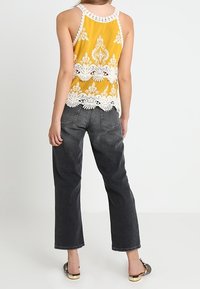 Keltainen pitsireunainen hihaton paita, jossa virkattu helma, yhdistettynä löysiin harmaisiin farkkuihin. Asusteina on tasapohjaiset, kuviolliset kengät.