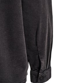 Dunkelgraues Langarmhemd mit glatter Textur, ausgestattet mit einem mit Knöpfen versehenen Manschetten und dezent gerafftem Stoff an der Schulter.