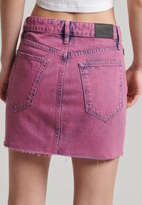 Rosa denim mini kjol med fransad nederkant, två bakfickor och en svart etikett vid midjan. Texturerad tyg med en blekt look.