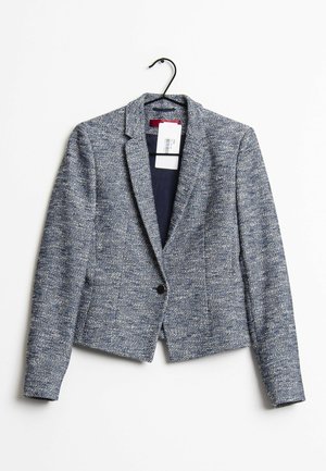 Niebiesko-biały, teksturowany damski blezer z jednym czarnym guzikiem, wiszący na czarnym wieszaku z widoczną metką cenową, na białym tle.