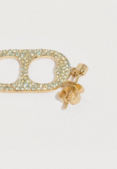 Zelta auskaru knaģis ar dubultu ovālu formu, rotāts ar mazām gaiši zilām un skaidrām kristāliem uz balta fona.