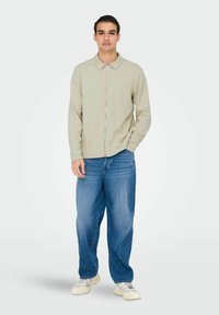 Light green zip-up shirt with a pointed collar, paired with loose-fitting blue denim jeans and light-colored sneakers. Smooth fabric texture.