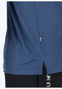 Camicia blu a maniche corte realizzata in tessuto testurizzato, con uno spacco laterale e un piccolo emblema della bandiera svedese giallo e blu all'orlo.
