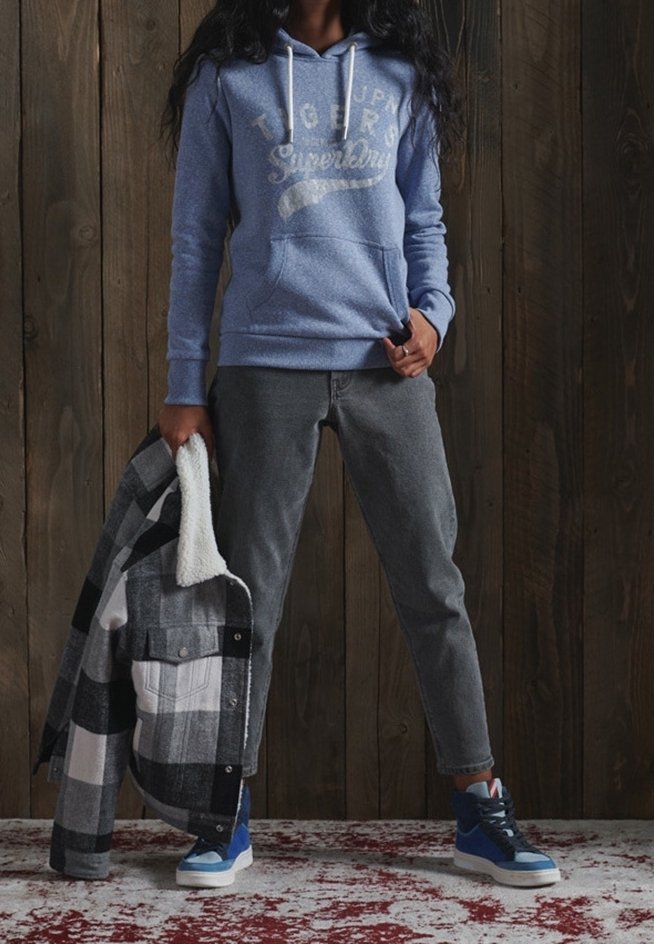 Sudadera azul con bolsillo frontal y cordones blancos, pantalones grises, chaqueta a cuadros en blanco y negro, y zapatillas azules con suelas blancas.