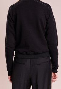 Felpa nera con maniche raglan, orlo e polsini a coste, caratterizzata da cuciture a contrasto sulle spalle e una texture morbida.