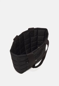 Mustassa tikatussa kangaskassissa on kangasvarret. Sisäpuolella on sileä vuori ja vetoketjullinen tasku. Ulkopuolella on teksturoitu, pehmustettu muotoilu.