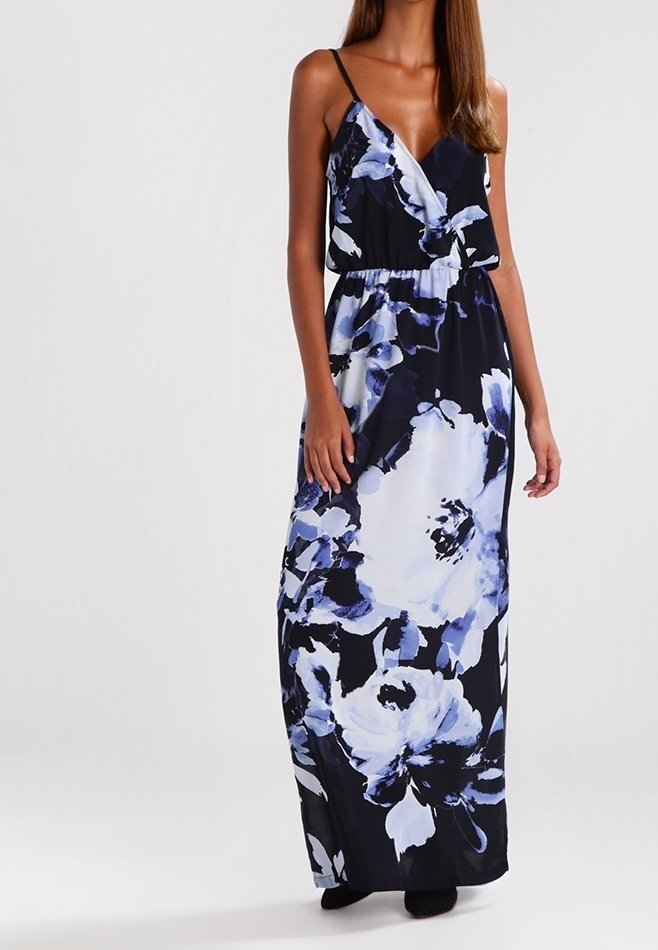 Femme portant une robe maxi noire sans manches avec un grand imprimé floral blanc et bleu et de fines bretelles.