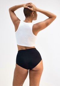 Vit ribbad crop top i kombination med högmidjade svarta underkläder. Släta texturer, enkel design och neutrala färger. Bakifrån.