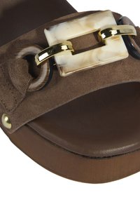 Bruine suède instapsandaal met een grote crème en gouden gesp, zwarte accenten en een gestructureerde bruine zool.