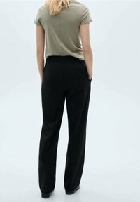 Pantalon noir à jambes larges avec poches avant, associé à un haut olive à manches courtes. Design minimaliste, texture lisse et coupe ajustée.