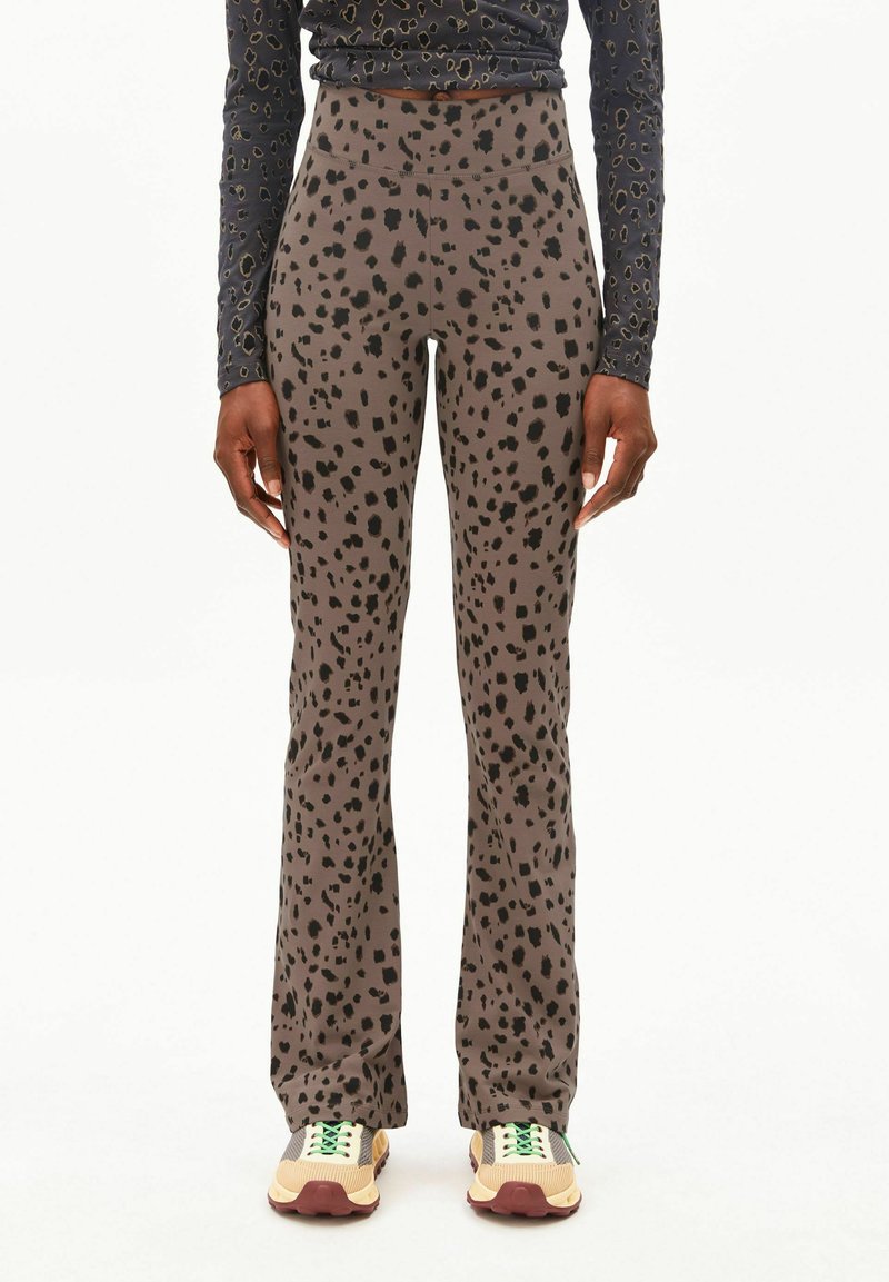 Leggings marron évasés avec un motif à pois noirs, fabriqués en tissu extensible. Assortis à des baskets beige et vert.