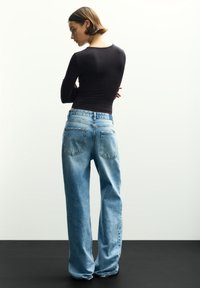 Schwarzes Langarmoberteil kombiniert mit hoch geschnittenen, weit geschnittenen hellblauen Jeans, die zwei Gesäßtaschen und eine ausgewaschene Textur aufweisen.