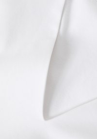 Tessuto di cotone bianco con una texture liscia, caratterizzato da un ritaglio triangolare. Il materiale appare leggero e drape in modo sottile.