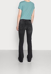 Upnuté, krátké rukávy, tyrkysové tričko spárované s černými, zvonovými džíny s objeveným nádechem a dvěma zadními kapsami.