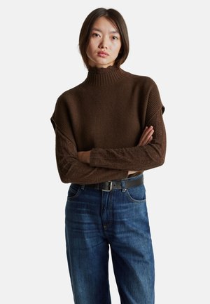 Bruine gebreide pullover met een hoge, ribbelige hals, korte mouwen en een gestructureerd lichaam, gecombineerd met blauwe jeans en een zwarte riem.