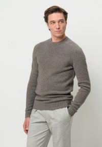 Maglione grigio a maglia con scollatura tonda e polsini e orlo a coste. Il tessuto appare morbido e textured, abbinato a pantaloni grigi chiari.