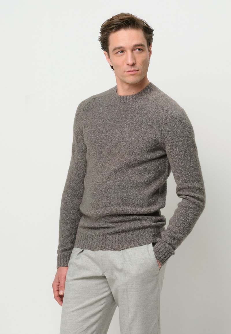 Maglione grigio a maglia con scollatura tonda e polsini e orlo a coste. Il tessuto appare morbido e textured, abbinato a pantaloni grigi chiari.