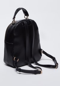 Sac à dos en cuir noir de forme arrondie, fermeture éclair, bretelles réglables et accents de quincaillerie dorée. Texture lisse avec un minimum de détails.