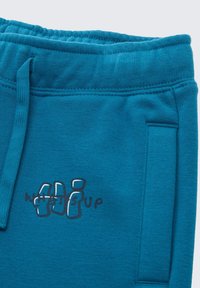 Turquoise fleecy joggingsbroeken met een elastische tailleband, voorzien van een kleine bedrukte opdruk met de tekst "WHATS UP" in het zwart. Zijzakdetails.