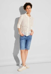 Vit skjorta med knappar och ögonlåtdekor vid nederkanten, i kombination med uppvikta denimshorts och ljusa sneakers. Enkelt, avslappnat sommaroutfit.