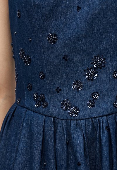 Σκούρο μπλε φόρεμα τζιν με σφηκοφωλιά στη μέση και διασκορπισμένες μικρές μαύρες παγιέτες σε σχήμα λουλουδιών στο μπούστο και την φούστα.