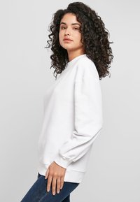 Baltas medvilninis džemperis su laisvu siluetu, ribštuotomis rankogaliais ir apačia. Lygi tekstūra, apvali iškirptė ir nuleistos peties siūlės.