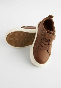 Brązowe syntetyczne skórzane sneakersy z białymi gumowymi podeszwami, z tradycyjnymi sznurówkami i rzepem. Teksturowana bieżnia na podeszwie.