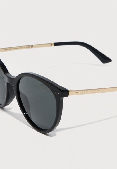 Γυαλιά ηλίου με μαύρο πλαίσιο, στρογγυλούς σκουρόχρωμους φακούς και χρυσούς βραχίονες με χαραγμένο το λογότυπο "Jimmy Choo".