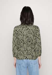 Grøn bluse med sort leopardprint, indsnævret talje, trekvartærmer og afslappet pasform, båret med lyseblå jeans.