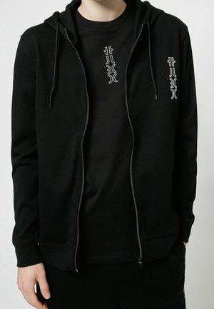 Schwarze Zip-Hoodie mit Kordelzügen, ausgestattet mit einem kontrastierenden weißen Grafikdruck auf der Brust. Weicher Stoff, enganliegende Bündchen und eine Kängurutasche.