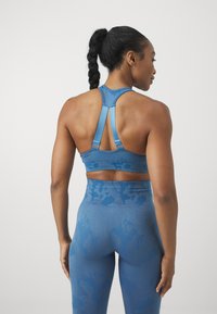 Sutiã desportivo azul com um design de costas cruzadas, apresentando alças ajustáveis e um acabamento texturizado. Combinado com leggings de cintura alta a condizer.