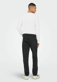 Jeans de mezclilla negra con un corte relajado, combinados con una camiseta de manga larga blanca. Los jeans cuentan con bolsillos traseros y una cintura estándar.