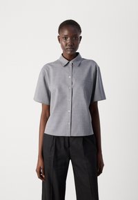 Gray short-sleeve button-up shirt with a collar, featuring a single chest pocket and a smooth, textured fabric. Worn with black pants.