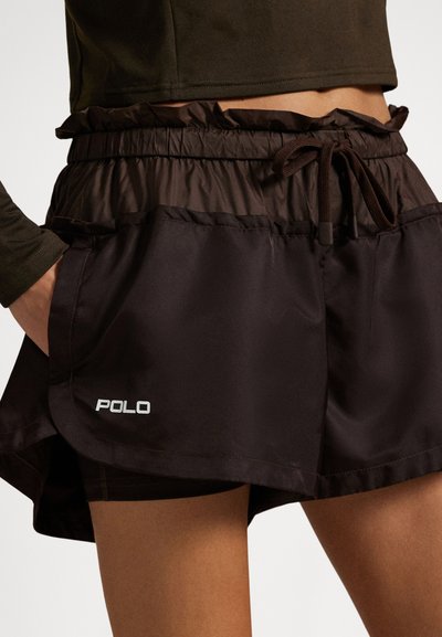 Εγγύς πλάνο ενός ατόμου που φοράει μαύρα αθλητικά σορτς με ελαστική μέση και κορδόνι, με λογότυπο "POLO" στο αριστερό πόδι.